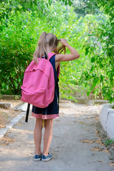 Back to school. A girl with school backpacks goes to school. The child walks near the school garden. students new year.