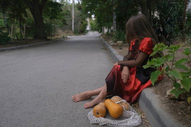 Cadılar Bayramı. Elinde balkabağı olan cadı kostümlü bir kız. Dışarıda kırmızı ve siyah cadı kostümlü bir çocuk var..