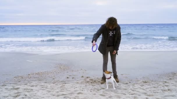 Ung man leker med sin hund på stranden slow motion — Stockvideo