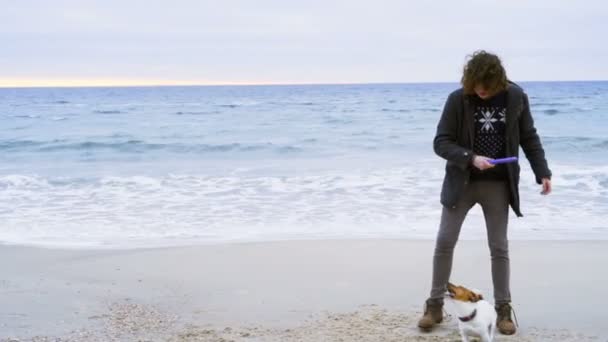 Joven hombre lanzar anillo juguete a su perro en la playa cámara lenta — Vídeo de stock