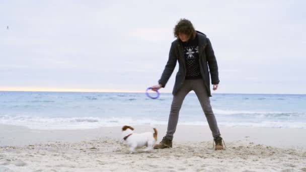 Joven hombre lanzar anillo juguete a su perro en la playa cámara lenta — Vídeo de stock