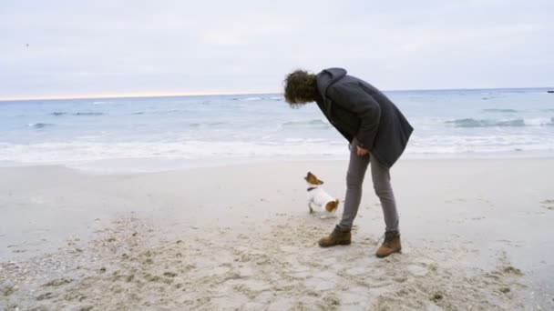 Jovem homem jogar anel brinquedo para seu cão na praia câmera lenta — Vídeo de Stock