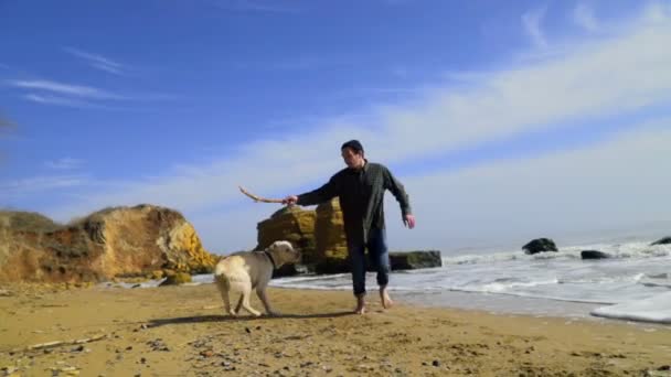 Νεαρός άνδρας παίζει με τον σκύλο του σε αργή κίνηση την παραλία — Αρχείο Βίντεο