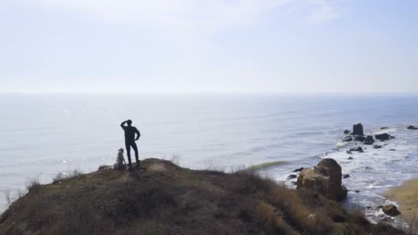 Uomo e cane che si arrampicano su una scogliera e guardano lontano nel mare slow motion — Video Stock