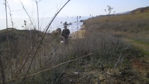 Uomo e cane che camminano su una collina vicino al mare al rallentatore — Video Stock