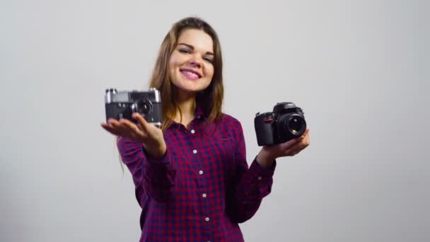 Молодая девушка предлагает зрителям разные камеры перед белой стеной — стоковое видео