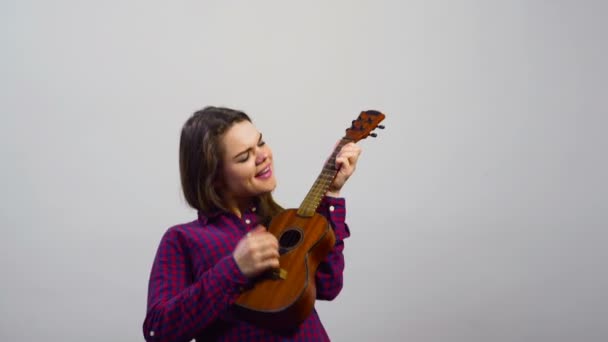 Giovane ragazza che gioca ukulele davanti al muro bianco — Video Stock