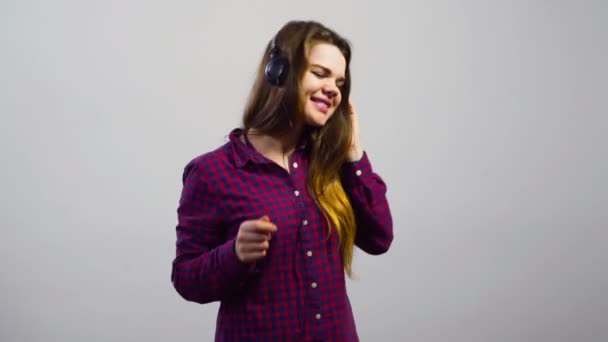 Ung flicka lyssna på musik med hörlurar och dansa framför vita väggen — Stockvideo