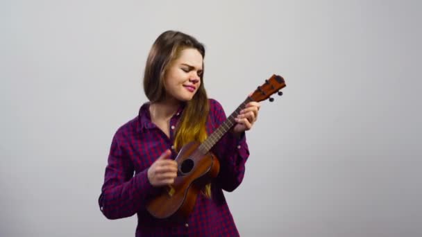 Mladá dívka hraje na ukulele před bílou zdí — Stock video