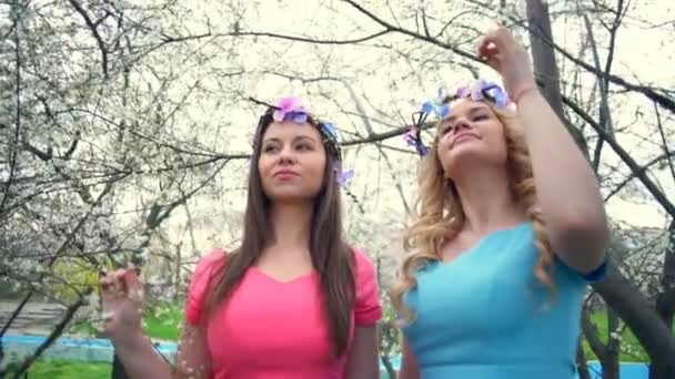 Две девушки, одетые в круги цветов, позируют в весеннем цветущем парке замедленной съемки. — стоковое видео