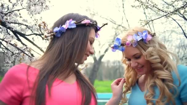 Two girls wearing circlets of flowers posing in spring blossom park slow motion — Stock Video