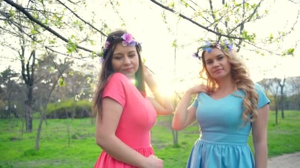Dos niñas con círculos de flores posando en el parque de flores de primavera cámara lenta — Vídeo de stock
