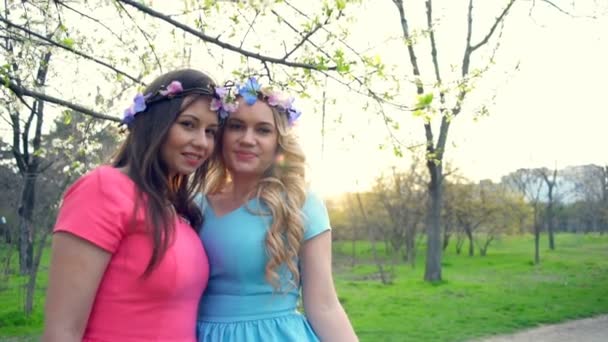 Dos niñas con círculos de flores posando en el parque de flores de primavera cámara lenta — Vídeo de stock