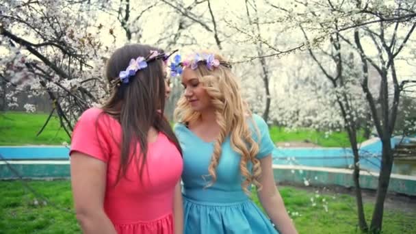 Duas meninas vestindo círculos de flores posando no parque de flores da primavera câmera lenta — Vídeo de Stock