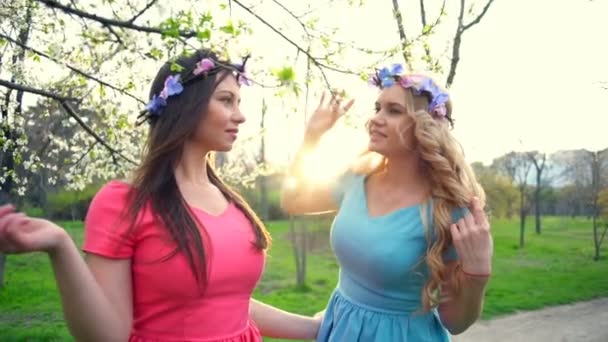 Две девушки, одетые в круги цветов, позируют в весеннем цветущем парке замедленной съемки. — стоковое видео
