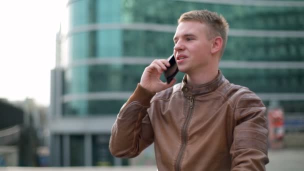 Ung man klädd i en läder jacka pratar i telefon i downtown slow motion — Stockvideo