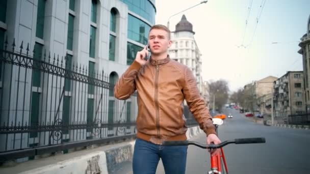 Разговаривая по телефону мужчина велосипедист прогулки рядом с велосипедом на улице замедленной съемки — стоковое видео