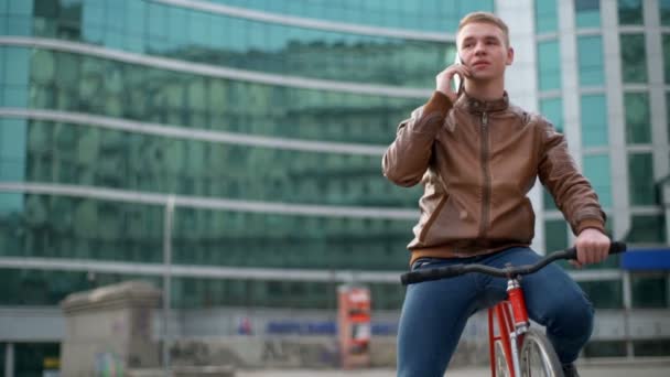 Jovem ciclista do sexo masculino fala ao telefone no centro da cidade câmera lenta — Vídeo de Stock