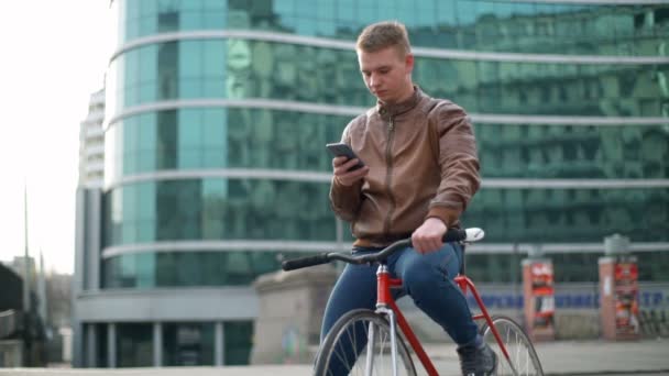 Jovem ciclista masculino usa um smartphone no centro da cidade em câmera lenta — Vídeo de Stock