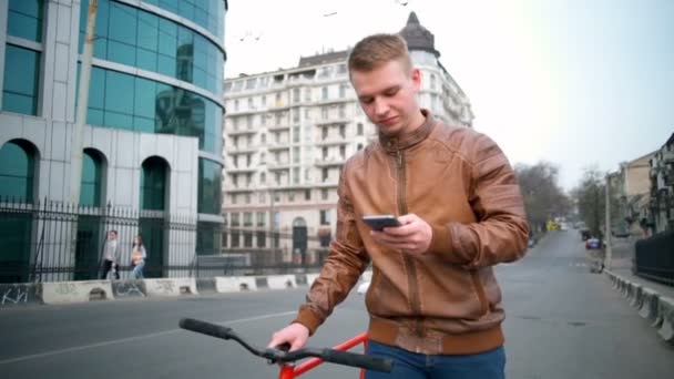 Usando um ciclista masculino smartphone caminha perto da bicicleta na rua câmera lenta — Vídeo de Stock