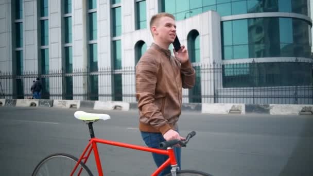 Разговаривая по телефону мужчина велосипедист прогулки рядом с велосипедом на улице замедленной съемки — стоковое видео