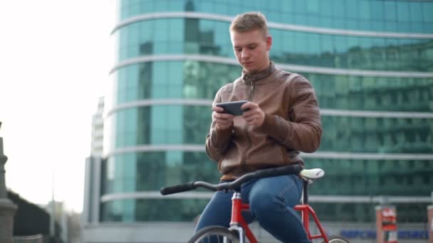 Young male bicyclist uses a smartphone in downtown slow motion — Stock Video