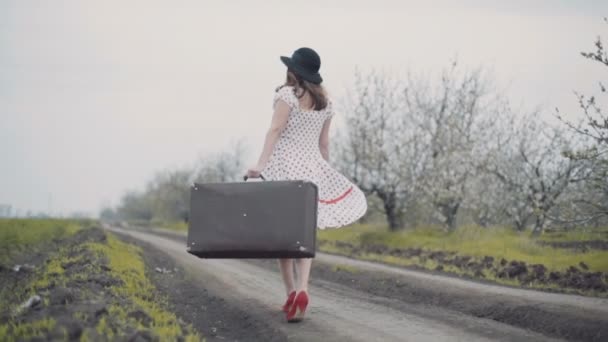 レトロなスタイルに身を包んだ若い女性動きが遅い国の道路の上を歩く — ストック動画