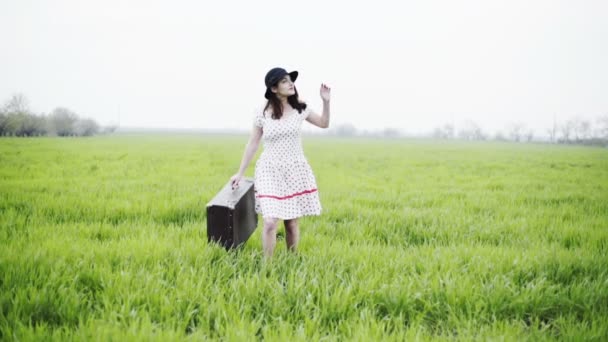 Vrouw gekleed in retro stijl draagt Bagage door de groene weide slow motion — Stockvideo