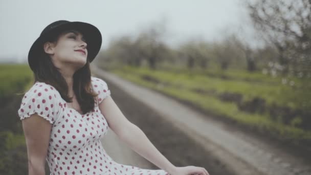 Mujer joven vestida en estilo retro sentada en la maleta en el camino del campo — Vídeos de Stock