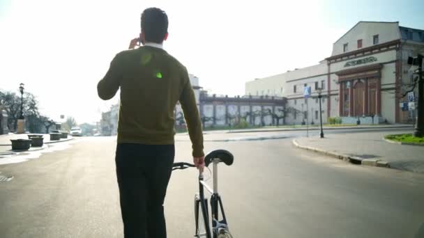 Indietro vista uomo va accanto alla bicicletta e parla al telefono rallentatore — Video Stock