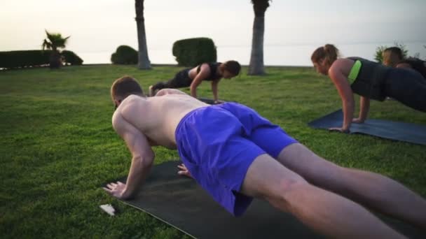 Skupina lidí, kteří dělají jógu na trávě u moře na úsvitu Zpomalený pohyb — Stock video