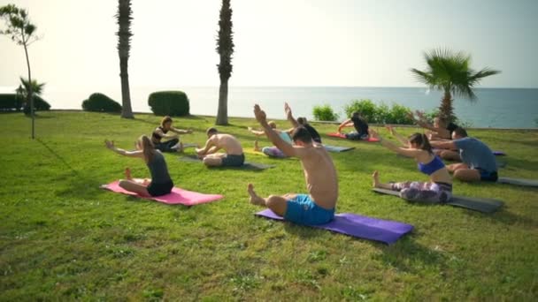 Grupo de personas practicando yoga en la hierba junto al mar cámara lenta — Vídeo de stock