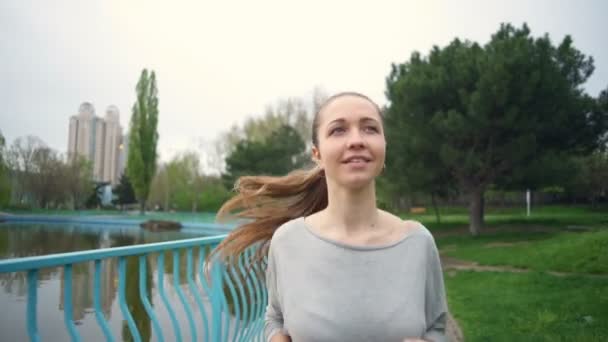 Lächelnde junge Frau läuft in Zeitlupe durch einen Park — Stockvideo