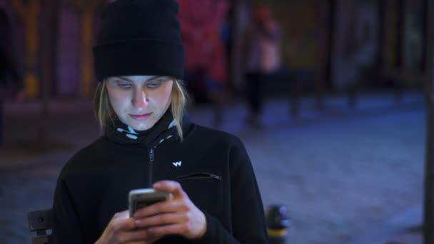 Fiatal nő egy okostelefon segítségével az esti utcán lassítva — Stock videók