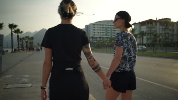 Two girls holding each other hands and walking along the road slow motion — Stock Video