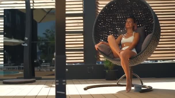 Mooie vrouw in bikini ontspannen in rotan stoel slowmotion ronde — Stockvideo
