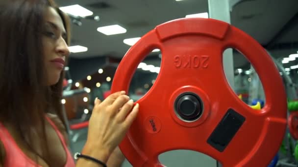 Close-up van aantrekkelijke vrouwelijke zet gewichten op barbell op de sportschool slow motion — Stockvideo