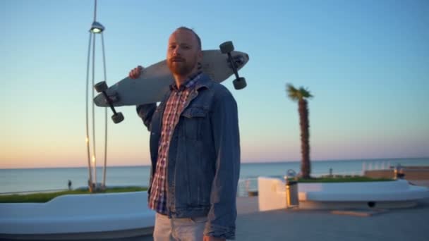 Câmera vai redondo homem segurando longboard no ombro câmera lenta — Vídeo de Stock