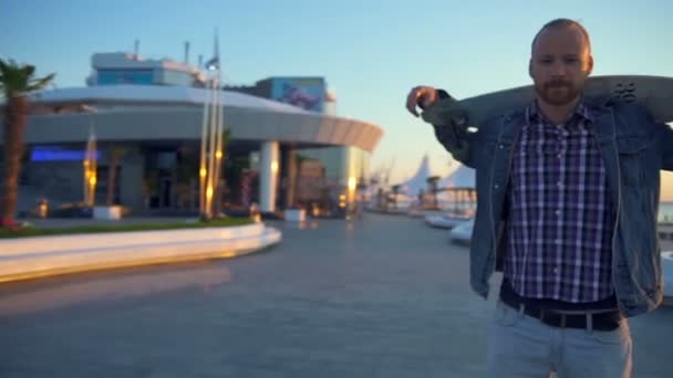 Kamera dreht Mann mit Longboard auf Schultern in Zeitlupe — Stockvideo