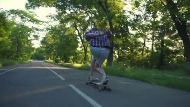Vue arrière de l'homme chevauchant longboard dans le parc par jour ensoleillé ralenti — Video