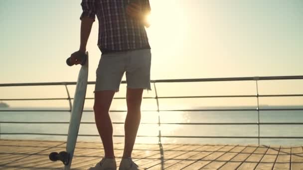 Bonito masculino segurando longboard e usando smartphone câmera lenta — Vídeo de Stock