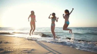 Üç genç mutlu kız yukarı ve aşağı deniz tarafı ağır çekim atlama