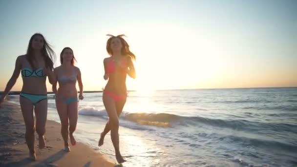 Tres chicas con bikini correr a lo largo del mar al amanecer cámara lenta — Vídeos de Stock