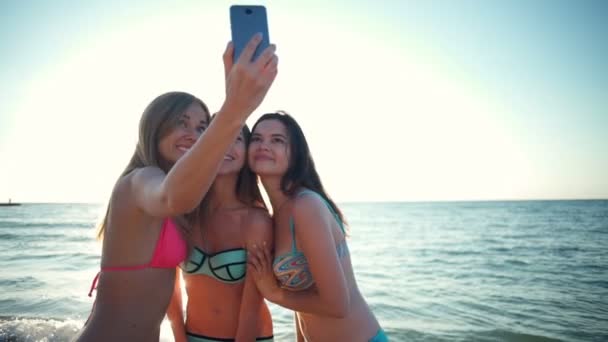 Tre unga kvinnor i badbyxor gör selfie på stranden slow motion — Stockvideo