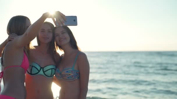 Tre glada tjejer på stranden gör selfie i sol ljus slow motion — Stockvideo