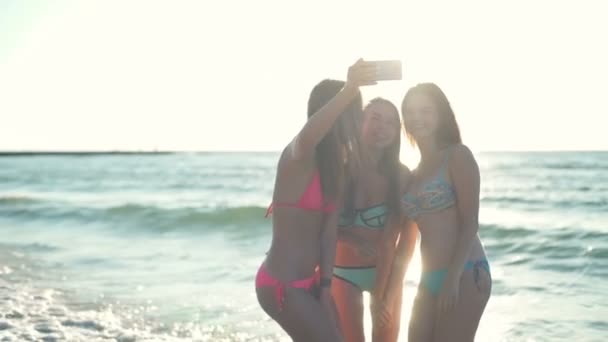 Chicas sonrientes en bikini tomando selfie en la luz del sol en la playa cámara lenta — Vídeos de Stock