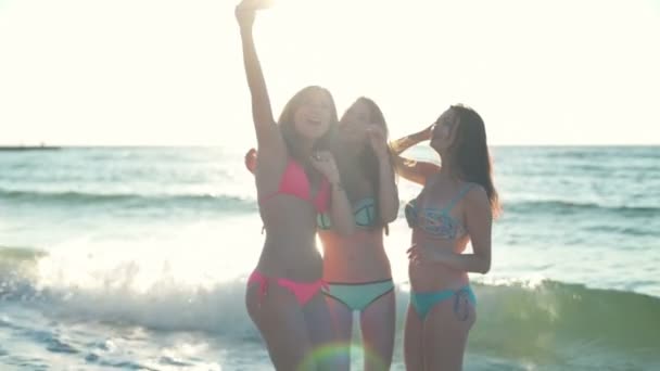 Tres mujeres jóvenes en bikini posando para selfie en el borde del mar cámara lenta — Vídeo de stock