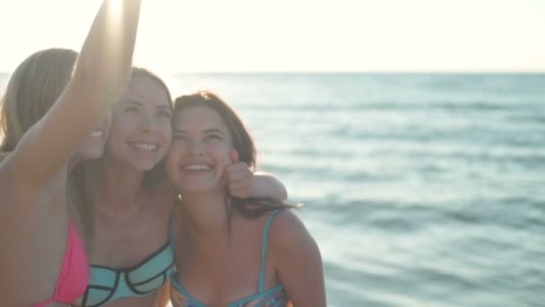 Tre ragazze gioiose in costume da bagno facendo selfie sulla spiaggia rallentatore — Video Stock