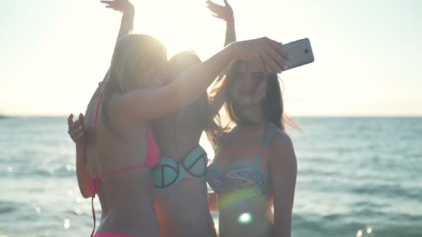 Drie gelukkige meisjes in bikini op het strand doen selfie zon licht vertraagd — Stockvideo