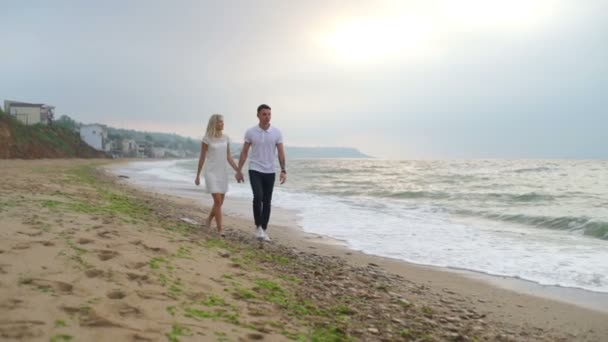 Vista frontal joven pareja cogida de la mano y caminando a lo largo del mar cámara lenta — Vídeo de stock